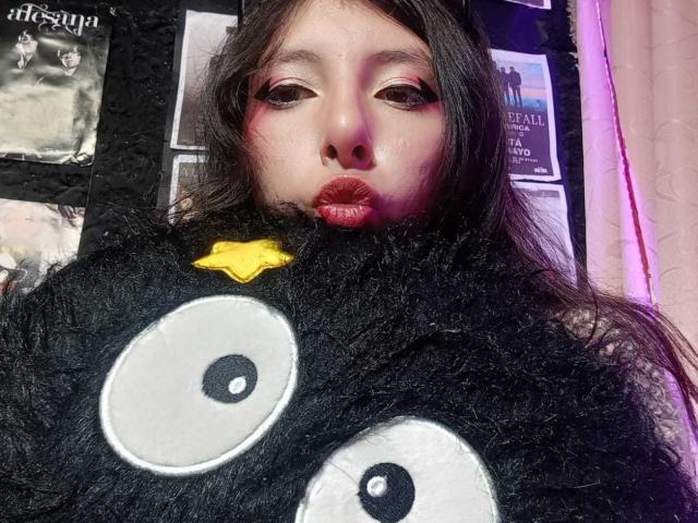ScarlettPrincess with puffy red lips, wearing a black fuzzy costume with large white eyes and a yellow nose, looking up at the camera. Long dark hair, subtle makeup.