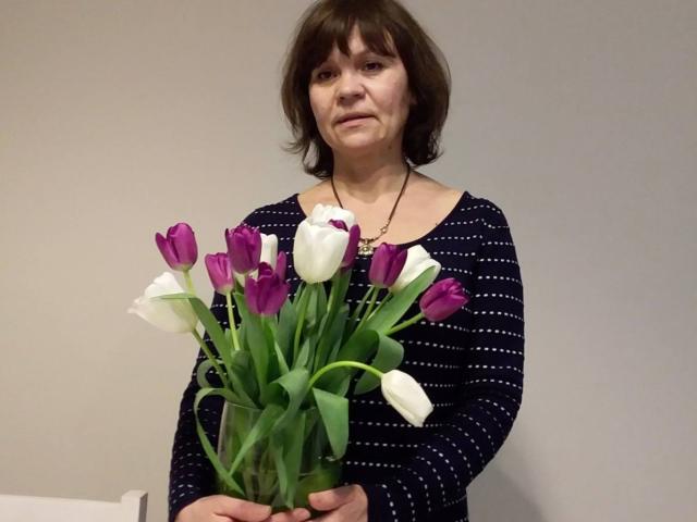 IngridWels with medium tits, brown bob, wearing a navy striped shirt, holding a bouquet of purple and white tulips in front of her.