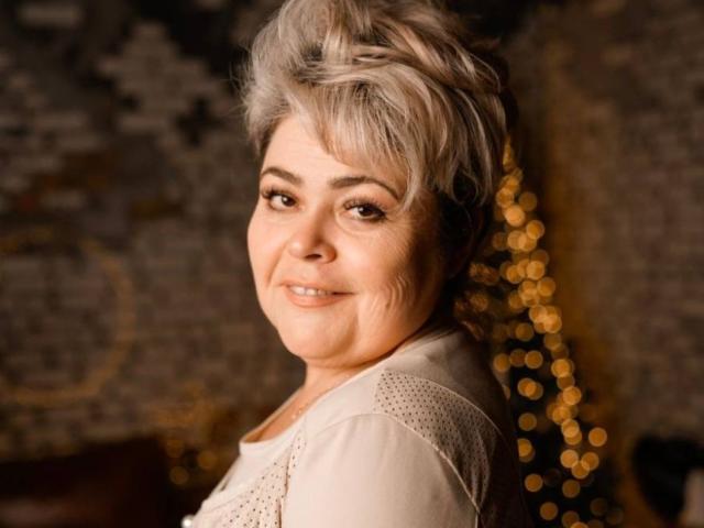 SabrinaPak, an older woman with short gray hair, smiling at the camera, wearing a white shirt with delicate patterns, her cute face showing gentle wrinkles.