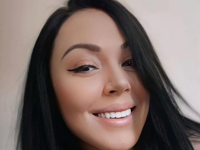 Layla84-hot tem cabelos pretos e escuros, um piercing fofo no nariz e um sorriso sexy com dentes brancos. Ela está olhando para a câmera com olhos meio fechados e sedutores, e sobrancelhas grossas..