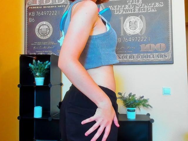 Steisii with a slim, toned body wearing a blue sports bra and black pants, hand on her butt, showing off her flat stomach and small, perky tits.