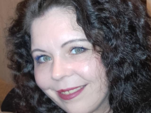 CarolFrankie with curly black hair, blue eyeliner, green eyes, and red lipstick, smiling at the camera, showing her cute, chubby face and pale skin.