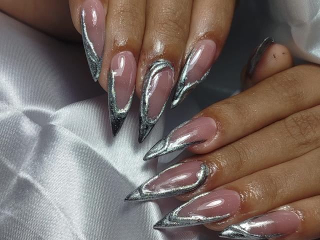 MyaaTyler's hands with long, pointed, silver-studded pink nails. Her fingers are slightly parted, showing off the shiny, metallic tips on each nail. Skin is smooth and dark.