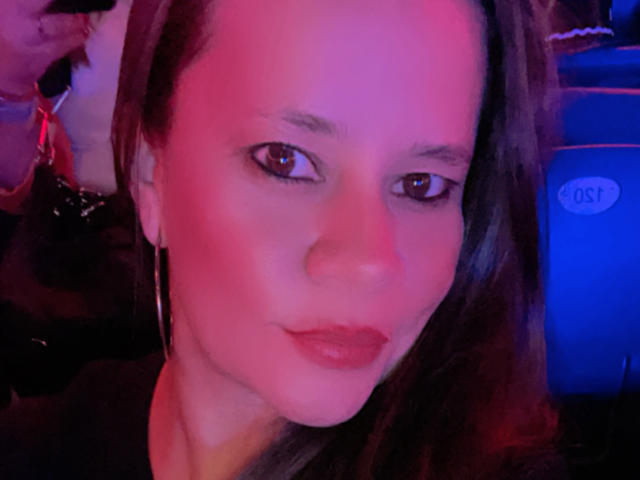 CharllotI's face with pink and blue lighting, brown eyes, slightly parted lips, wearing large hoop earrings, and a subtle smile. Her ass is not visible.