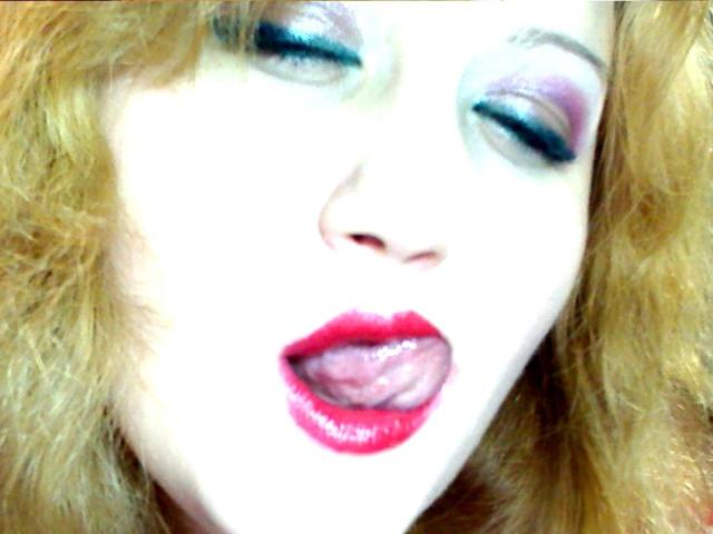 SeductiveBodyX's face with white skin, red lipstick, tongue out, purple eyeshadow, and wavy blonde hair, eyes partially closed, looking sexy and provocative.