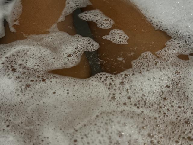Foamy, bubbly soap covering EricaLust's tan, hairy crotch in a dirty, brownish water bath. White, frothy bubbles surround EricaLust's exposed genitals.