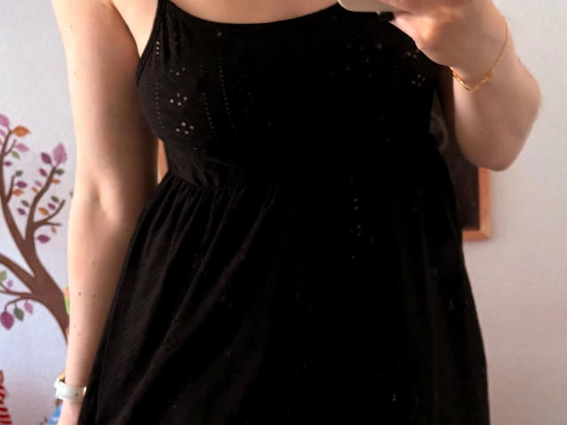Redhead88-hot trägt ein schwarzes Kleid mit kleinen weißen Punkten, hält ein Telefon, zeigt ihre Brüste, hat helle Haut, ein goldenes Armband und ein weißes Armband, in einem gut beleuchteten Raum..