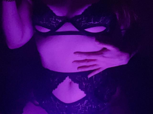 MiiS with purple-lit skin, wearing black lace lingerie, has hand on belly, showing cut-out bra and matching lace panties, showcasing small, firm tits and a sexy, curvy figure.