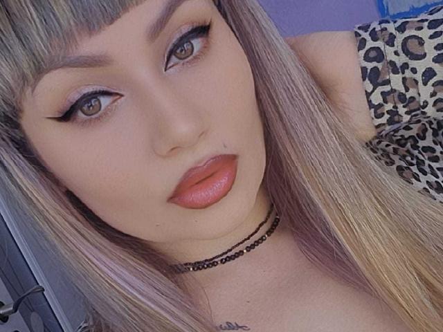 MirayDesire tiene el cabello rubio, ojos marrones, delineador de ojos alado, lápiz labial rojo y una blusa con estampado de leopardo. Lleva un collar negro con un tatuaje discreto en el cuello..