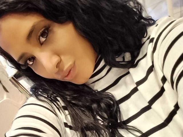 MariaCatalina with wavy black hair, brown eyes, and light skin, wearing a striped black and white shirt, looking at the camera with a slight pout.