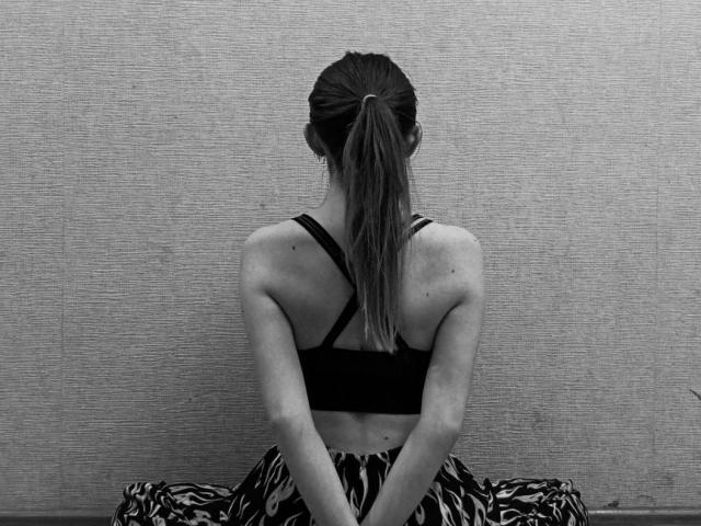 AvaMystic, with her back to the camera, has a ponytail, wearing a black sports bra and zebra-patterned pants, showing her muscular arms and small ass. Black-and-white photo.