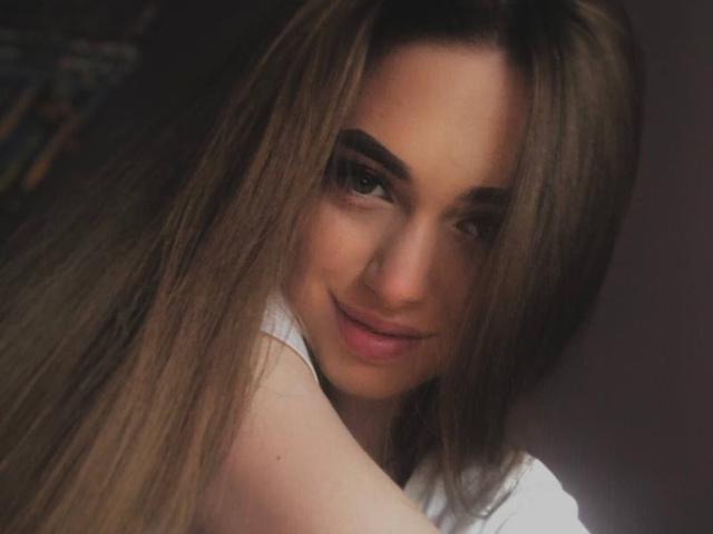 GoGoDream, con lunghi capelli castani, sopracciglia folte e un leggero sorriso, mostra un viso carino e labbra rosa pallido, indossando una maglietta bianca..