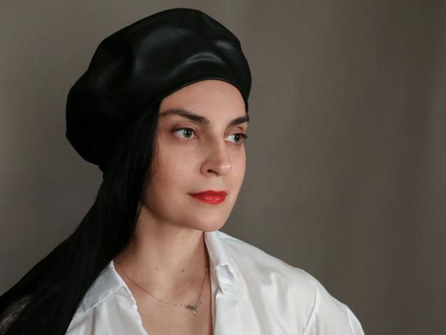 Xrystal-hot with black leather hat, white shirt, red lipstick, and long black hair, wearing a delicate necklace, looking slightly to the side.