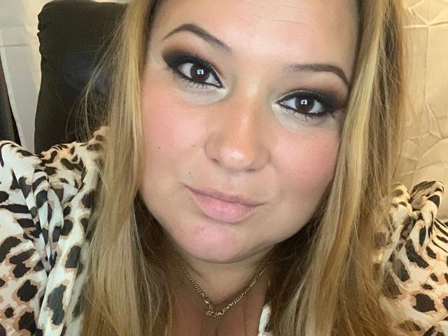 LaVa24-hot with pouty lips, blonde hair, heavy black eyeliner, and a leopard print top, wearing a gold necklace, looking directly at the camera with a slightly smug expression.