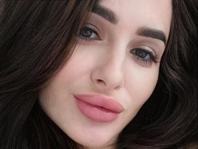 Saminaa's face with pink, plump lips, dark brown wavy hair, thick eyebrows, and blue eyes, looking slightly to the right with a subtle, confident smile.