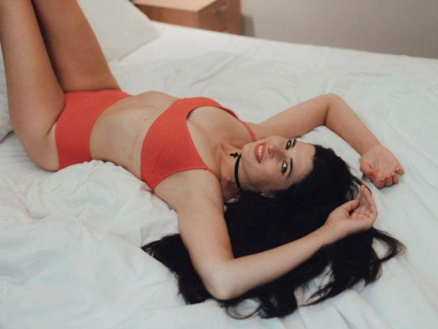 DarkWhiskers-hot with red bra and panties, lying on white bed, arms above head, long black hair, red lipstick, black choker, smiling, legs up, pale skin, sexy, attractive.