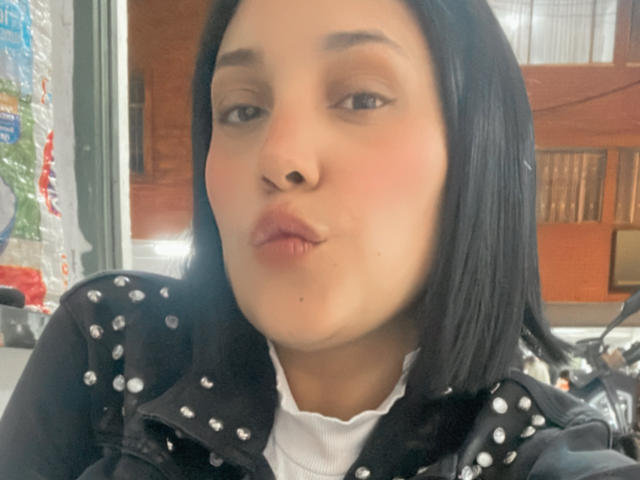 Samanta Muller, con cabello negro hasta los hombros, labios rosados y voluminosos, vistiendo una chaqueta negra con tachuelas, piel marrón clara, mejillas ligeramente sonrojadas y una camisa blanca, en un selfie..