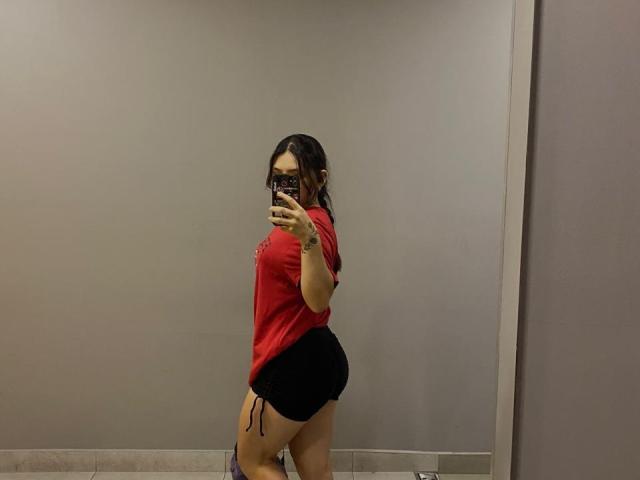 SophiaMarx with black shorts, red top, and a tattoo on her right arm, showing her big ass in a mirror selfie. Her phone has a colorful case.