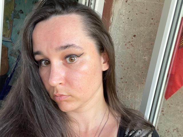 SaliBerry has brown eyes, straight brown hair, and a slightly flushed, pimpled face. She's wearing black with a shiny pattern, and her lips are in a neutral pout.