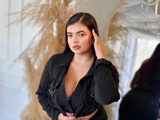 LaraJames with dark hair, black shirt, and cleavage, hand in hair, looking at camera, soft light, puffy lips, sexy, mirror reflection, chandelier, puffy ass, cute, stylish.