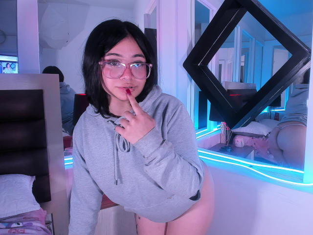 AmaraKazumi with black hair, glasses, and gray hoodie, finger in mouth, no pants, showing her ass in mirror reflection, neon blue lights, cute, sexy, bedroom, seductive.