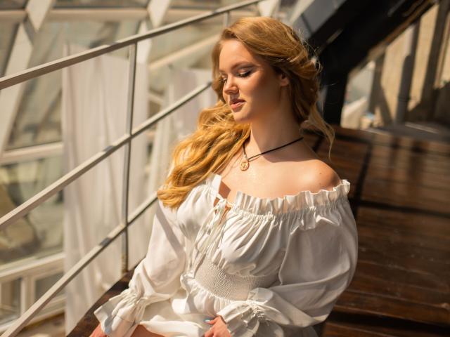 CelesteNoirr with long blonde hair, white off-shoulder dress, and black necklace, sitting on wooden stairs, sunlight on her face, gentle smile, soft light, relaxed, pretty.