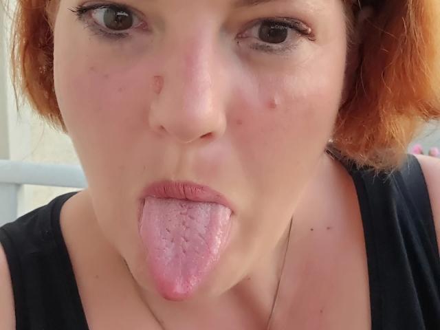Joyfull-hot a les cheveux roux, la peau pâle, et elle sort sa langue rose, avec une petite bouton sur le nez. Elle porte un haut noir et a du crayon pour les yeux..