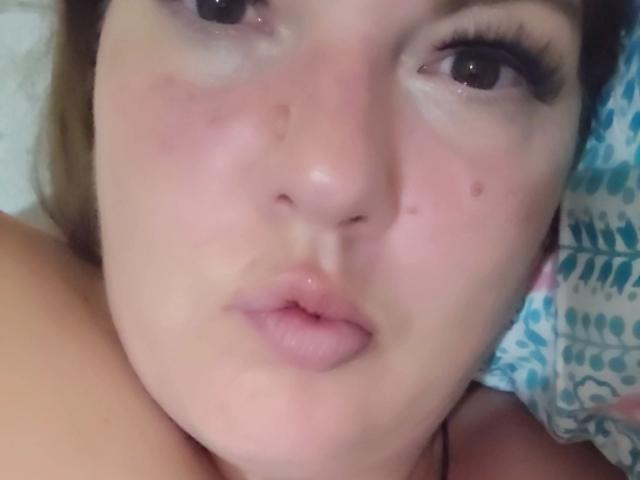Joyfull-hots Gesicht, mit rosafarbener Haut, einem kleinen Pickel auf der Nase, leicht geöffneten, glänzenden, rosafarbenen Lippen und braunen Augen mit dicken Wimpern, liegt auf einem blauen Kissen mit Muster..