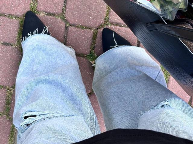 Barberry's frayed, light blue jeans with black pointed-toe shoes, showing slight tears near the knees, standing on red brick pavement. Black shoe on the left, black shoe on right.