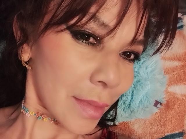 SamaraBellet has a cute face with dark brown eyes, sparkly eyeshadow, pink lipstick, and a colorful bead necklace. Her brown hair has bangs, and she wears small gold earrings.