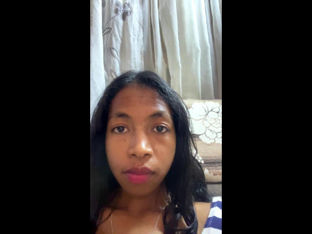 ChocolatGoodGirl has medium brown skin, black wavy hair, pink lipstick, and is wearing a striped top, looking straight at the camera with a neutral expression.