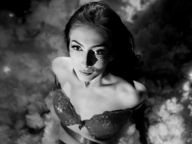 Black-and-white photo of AnyaLobb with freckles, looking up, wearing a sparkly bra, her tits slightly visible, dark hair, and a shadow on her face.