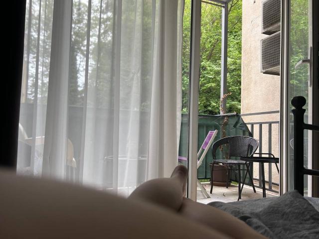 SweetLime's bare tits and soft pink nipples are visible in the foreground, lying on a bed with white curtains in the background, and a balcony with chairs outside.