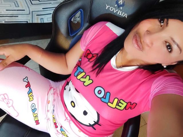 EstrellaSmmith, com seios médios, vestindo uma camiseta rosa do Hello Kitty e calças rosa do Hello Kitty, sentada em uma cadeira preta Yovia, tirando uma selfie, com cabelo preto e liso..