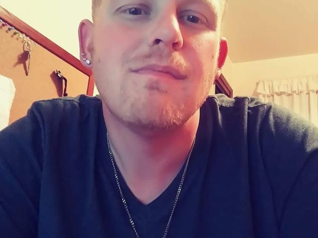 FresherDanny, con una leggera barba e capelli biondi corti, indossa una maglietta nera e una collana d'argento, ha un leggero sorriso e un piercing al naso in un selfie..