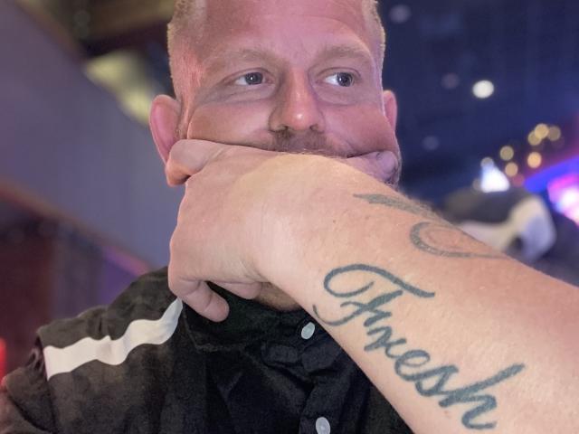 Il viso di FresherDanny è delicatamente sorretto da una mano tatuata con la scritta "Faresh", il suo naso è leggermente schiacciato, indossa una maglietta nera con strisce bianche..