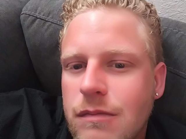Danny, mit kurzen, lockigen blonden Haaren, einer kleinen Nase, heller Haut und einem kleinen Bart, trägt ein schwarzes Hemd und hat ein Ohrpiercing..