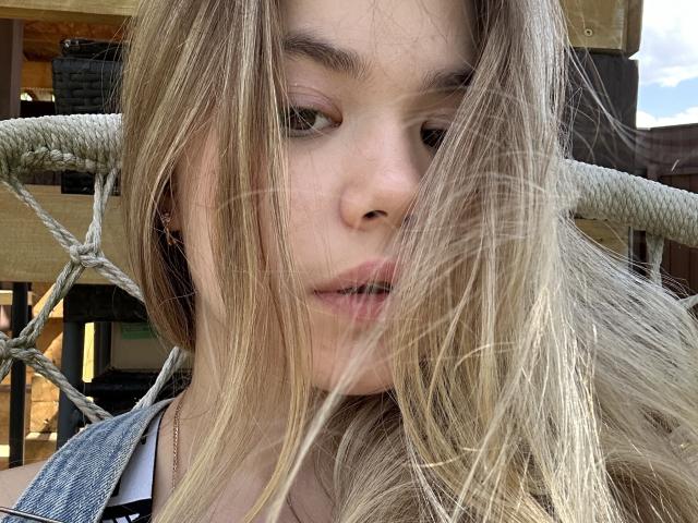 SweetLime has blonde hair, a neutral expression, and is partially covered by strands of her hair. She's wearing denim and has a rope in the background.