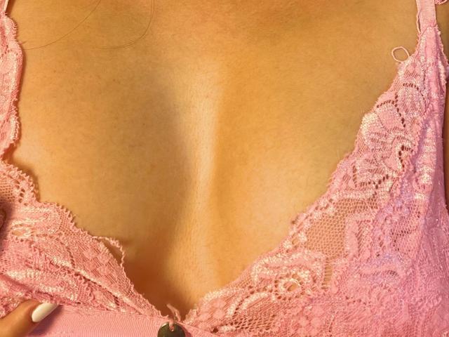 KateOwens' tits in a pink lace bra, showing her cleavage and slightly tanned skin. Her fingers with nude nails are just below the lace.