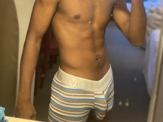 KingBlaze's toned, dark-skinned torso with visible abs, wearing striped white, blue, and gray boxer briefs, holding a phone to take a mirror selfie.
