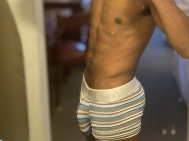 KingBlaze's slim, muscular, dark brown body wearing striped white, blue, and gray Calvin Klein briefs, showing a defined ass and a small tattoo on the right side.