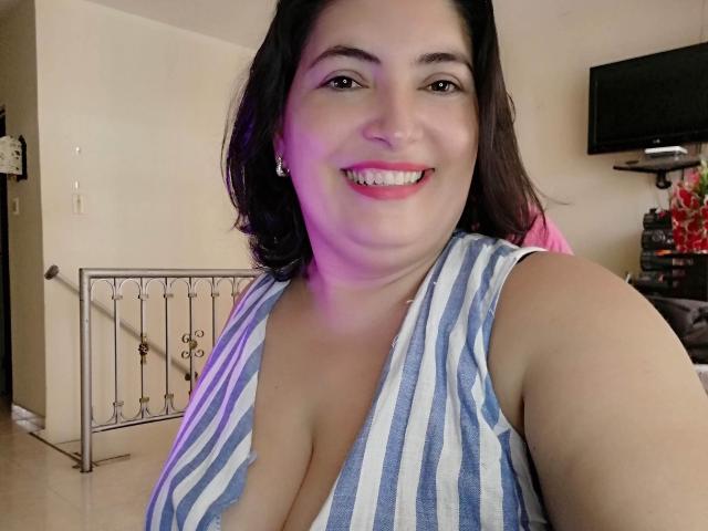 Lina69s has large tits in a blue and white striped top, smiling with pink lipstick, dark brown hair, and a cute face, in a selfie with purple lighting.