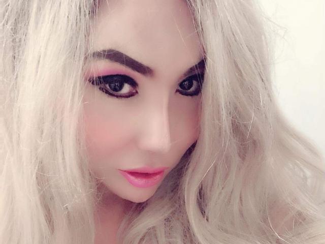 QueenFhukelya has platinum blonde hair, pink eyeshadow, black eyeliner, and pink lipstick. Her eyes are looking directly at the camera with a slight, sexy, and confident smile.