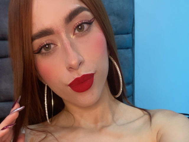 SarahLuxe with red lipstick, hoop earrings, and long brown hair, pouting with glossy eyes and pink blush. She has a slim neck and visible collarbones.