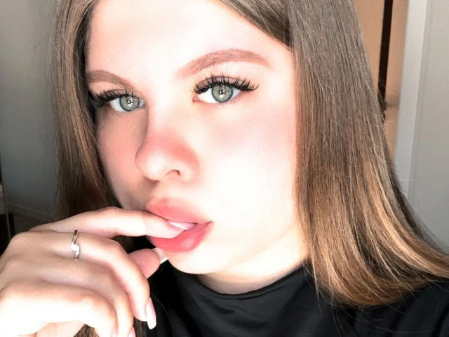 AbbyMaus-hot with pouty pink lips, finger in mouth, gray eyes, long brown hair, black shirt, ring on finger, pale skin, looking at camera, sexy.