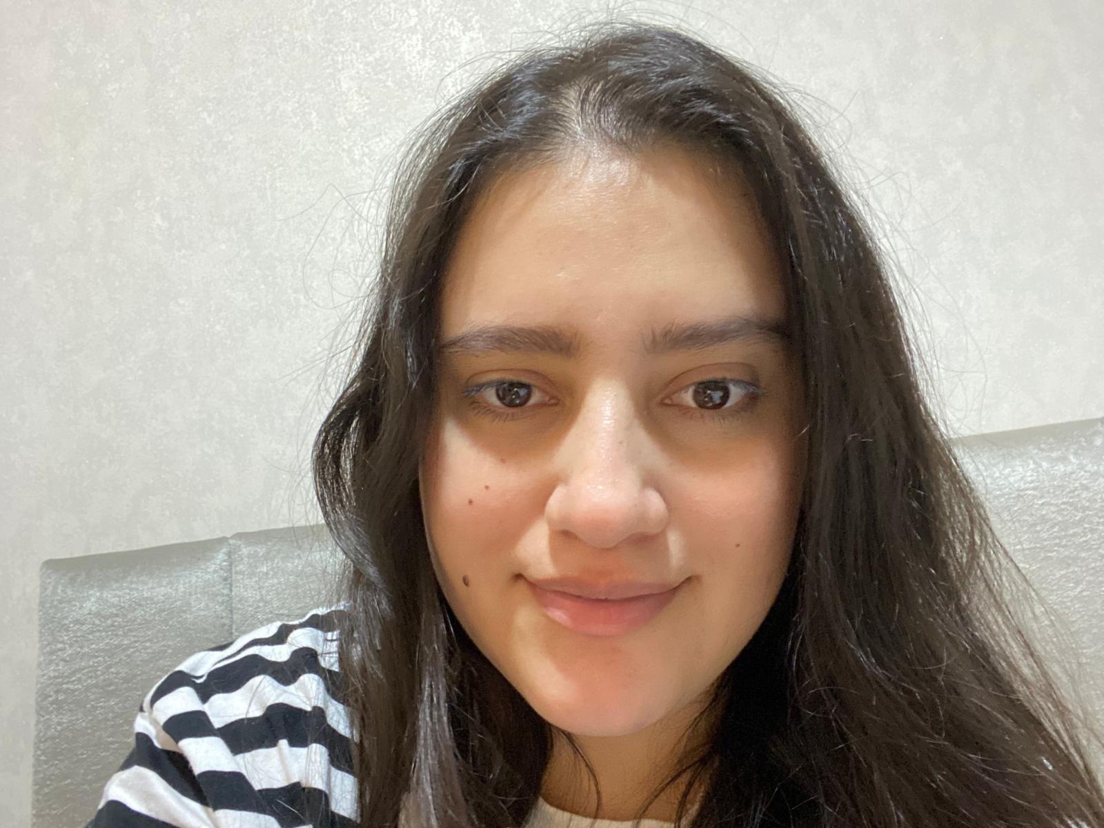 HottNicki tiene el cabello largo, oscuro y ondulado, ojos marrones y una pequeña peca en la mejilla derecha. Lleva una camisa a rayas negras y blancas y sonríe suavemente..