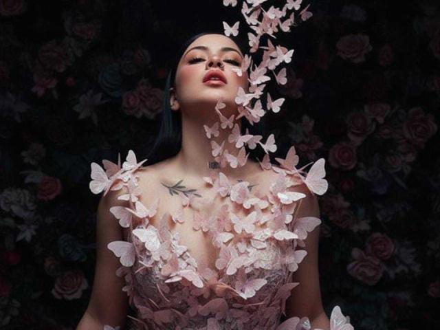 EmmieX with blue hair, wearing a pink lace dress, surrounded by floating pink butterflies, has a butterfly tattoo on her chest, eyes closed, lips slightly parted, dark background.