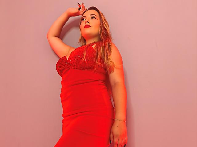 ZoeTobon69 with red dress, sequined top, and red lipstick, arm raised, looking up, blonde hair, fair skin, curvy, standing, red light, bracelet, confident, sexy.