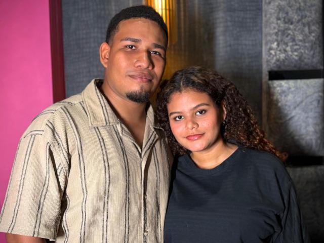 LucasandSasha, a chubby brown dude with a goatee, and Sasha, a curly-haired brown chick with small tits, standing close, smiling, and looking at the camera.