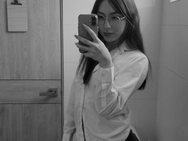 Luluberrie with long dark hair, glasses, and white button-up shirt takes a mirror selfie with a phone in a bathroom. Her tits are small, and her ass is unseen.